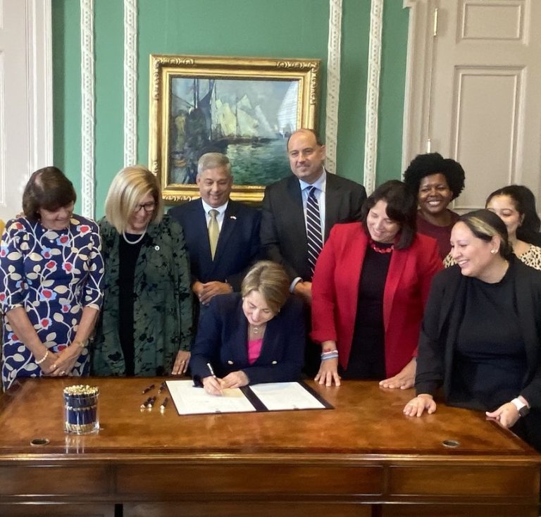photo of a group of eight people watching a white woman politician sign a document